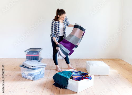 A young woman puts away seasonal clothes and items for storage in boxes. Spring cleaning