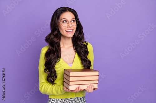 Photo of optimistic nice brunette curly lady look empty space hold books wear spectacles green sweater isolated on purple background