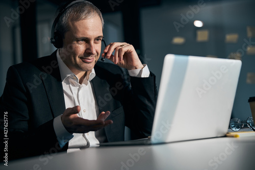 Joyful man in headphones using laptop at work