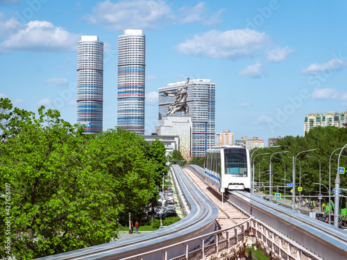 The Moscow monorail train follows the overpass at VDNKh. Famous sculpture  Worker and Kolkhoznitza Woman  and residential skyscrapers in the distance. City landscape. Transport system of Moscow