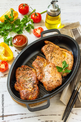 Barbecues parties menu. Baked meat pork loin on the bone with spices in a cast iron pan on rustic wooden table.