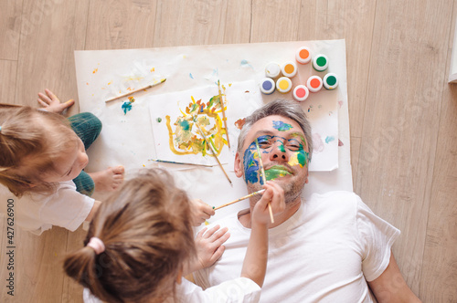 happy dad is lying on the floor, the children paint his face with watercolors. father's day