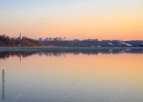 Cityscape at golden sunset with buildings reflecting in the lake. Early spring season and remainings of semi-melted ice.