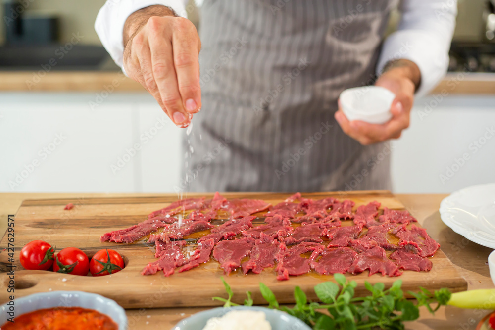 A close-up of the chef's hands adding salt to the carpaccio meat
