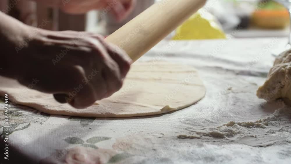 A woman rolls out the dough with a rolling pin.Hands close up, slow motion.