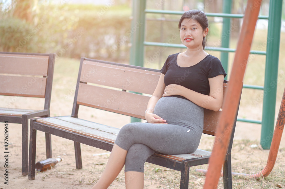 A pregnant woman sits on the garden table with her hand on her stomach. A pregnant woman sits on the garden table with her hand on her stomach.