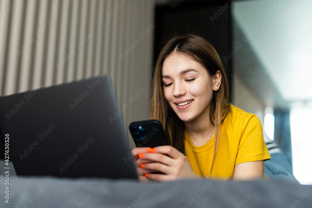 Portrait of beautiful young woman using her mobile phone in the bed with laptop. Portrait of beautiful young woman using her mobile phone in the bed with laptop.