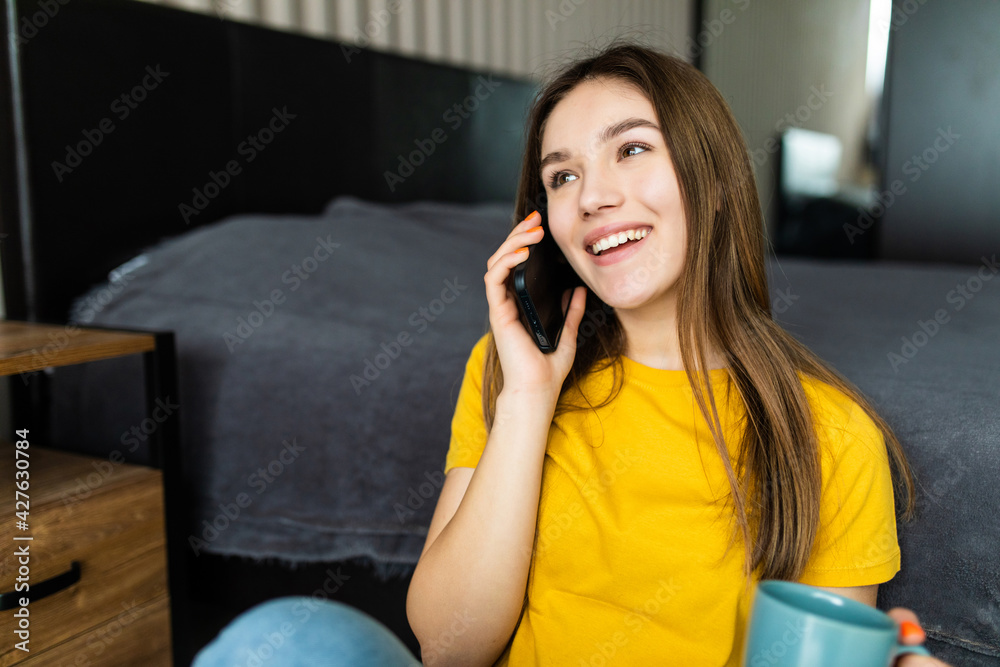Young woman calling on mobile sitting on floor. Serious woman talking on phone and drinking coffee, having rest, copy space Young woman calling on mobile sitting on floor. Serious woman talking on phone and drinking coffee, having rest, copy space