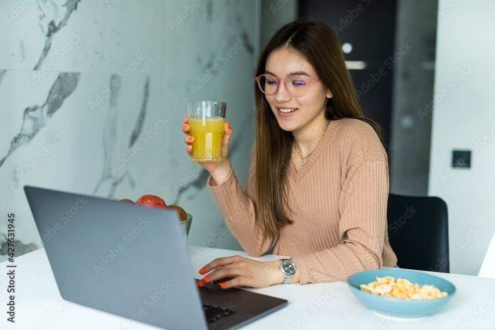 Image of a beautiful young woman at the kitchen indoors at home using laptop have a dinner watch videos. Image of a beautiful young woman at the kitchen indoors at home using laptop have a dinner watch videos.