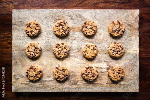 Freshly baked chocolate chip cookies on a wooden board on dark and moody wooden background