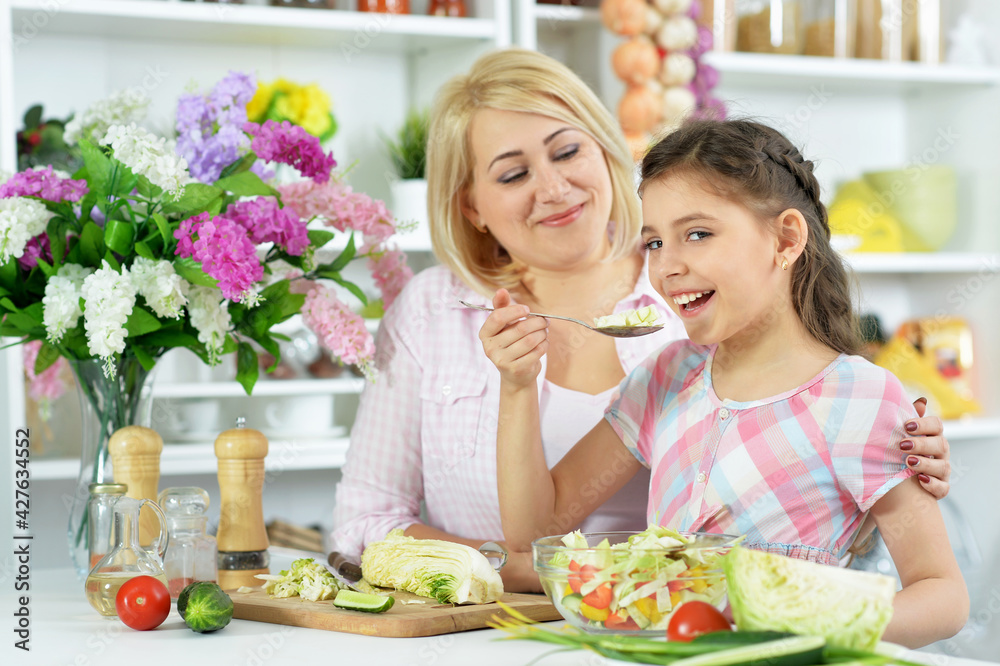 Cute little girl with her mother cooking together at kitchen table