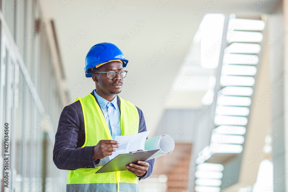 Quality controller in factory. Portrait of smiling engineer in hardhat standing at construction site holding blueprint. Happy male architect writing on clipboard Quality controller in factory. Portrait of smiling engineer in hardhat standing at construction site holding blueprint. Happy male architect writing on clipboard