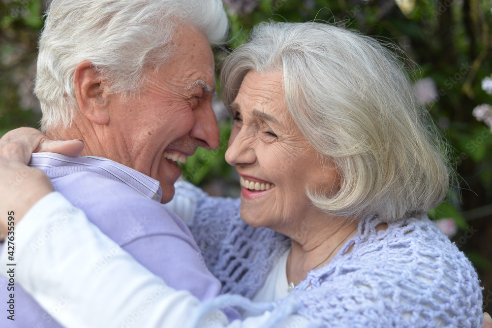 portrait of beautiful senior couple hugging  by lilacs   in the park