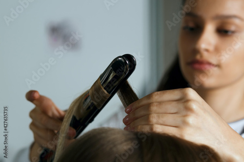 Hair stylist making hairstyle with iron