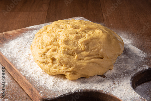 Dough being sprinkled with wheat on wood, selective focus.
