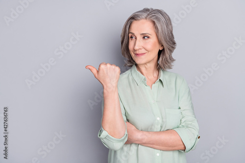 Photo of happy positive smiling dreaming mature woman point finger copyspace advertisement isolated on grey color background