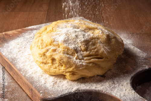 Dough being sprinkled with wheat on wood, selective focus.