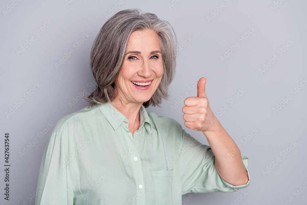 Photo of happy smiling good looking pretty granny showing thumb-up like approval isolated on grey color background Photo of happy smiling good looking pretty granny showing thumb-up like approval isolated on grey color background