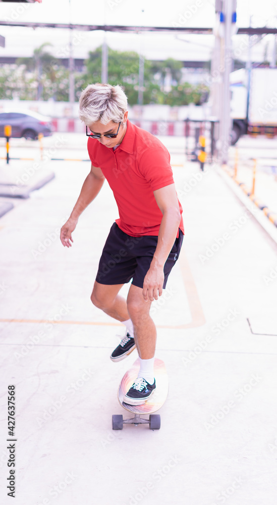 Asian handsome man surfing skateboard at skateboard street way in daylight time, summer holiday