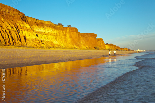 Portugal. Beautiful seascape of sandy Praia da Falesia beach in Algarve with unusual terracotta sculptural rocks attracts tourists for a seaside vacation. Summer family holidays. People out of focus photo