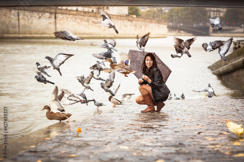 A woman with an umbrella feeds birds on the embankment of the river