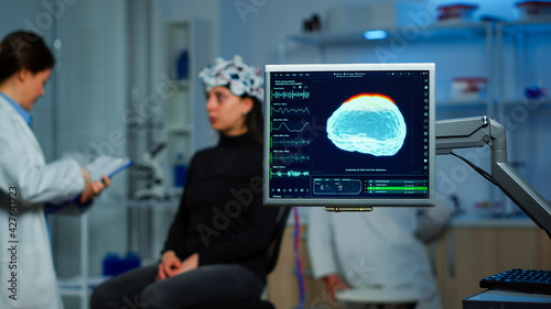 Neurologist doctor analysing nervous system using eeg headset scanning woman brain. Scientist researcher using high tech developing neurological innovation, monitoring side effects on monitor screen photo
