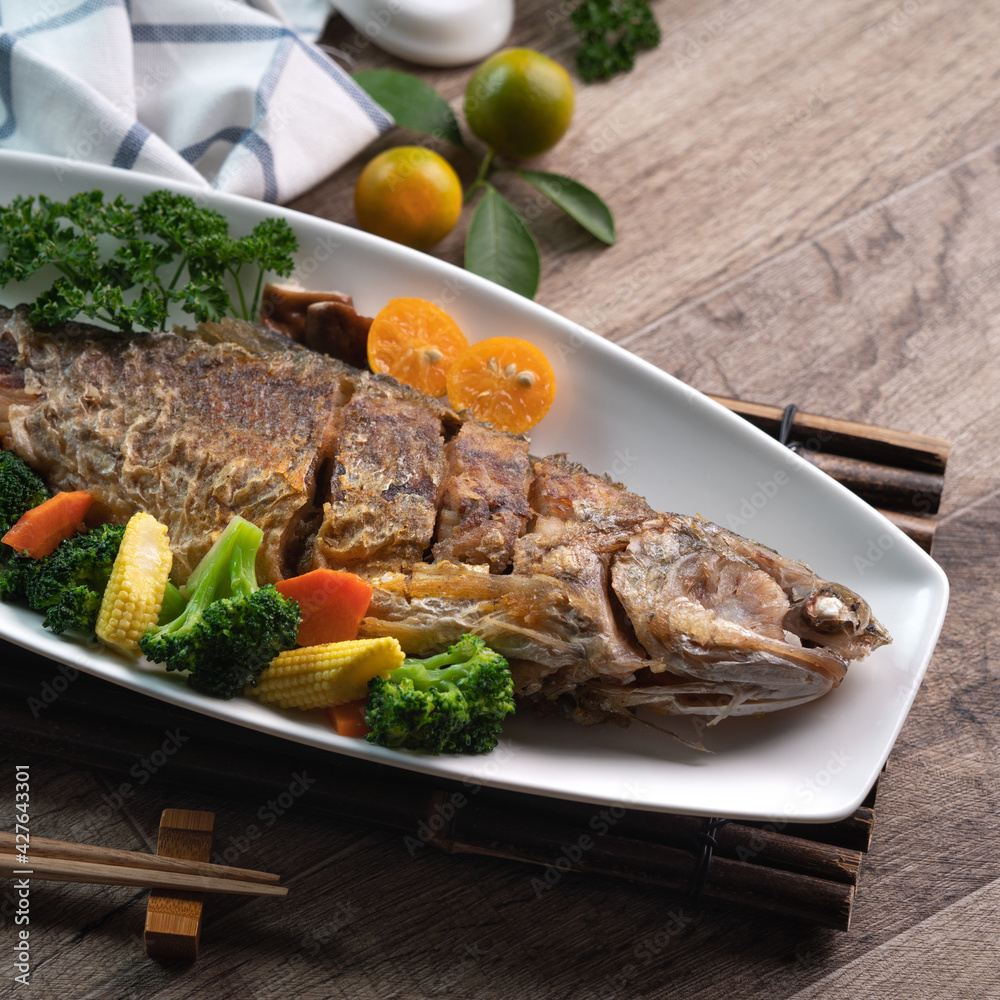 Close up of delicious pan-fried fish dish in a white plate with vegetable. Close up of delicious pan-fried fish dish in a white plate with vegetable.