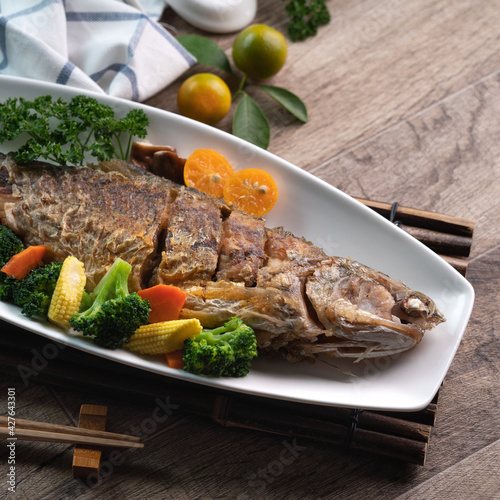 Close up of delicious pan-fried fish dish in a white plate with vegetable. photo