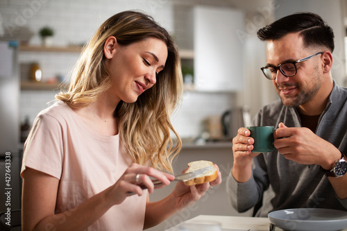 Beautiful woman enjoying in breakfast with boyfriend. Happy young couple drinking coffee and eating sandwich at home.