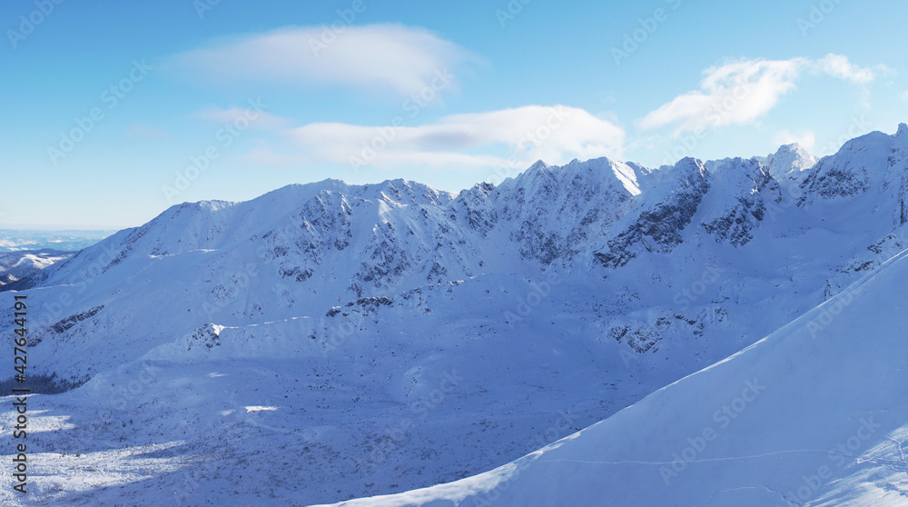 Fototapeta premium Picturesque view of the snow-covered mountains against a blue cloudy sky during the winter season with mountain peaks touching the sky in the city of Zakopane - Kasprowy Wierch 
