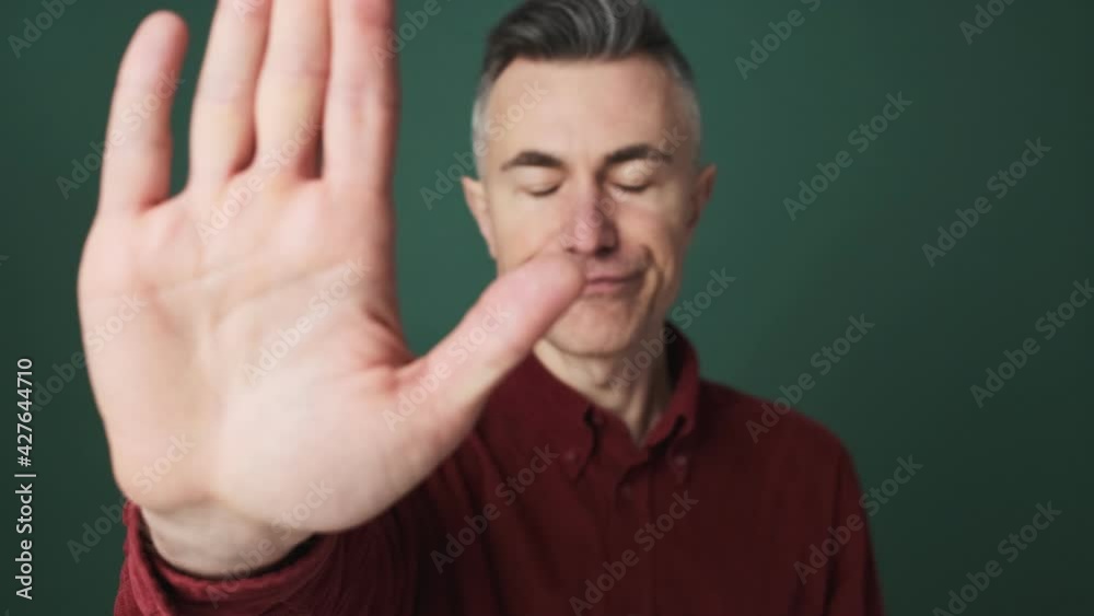 A close-up view of a serious elder man is doing stop gesture standing isolated over green background in the studio A close-up view of a serious elder man is doing stop gesture standing isolated over green background in the studio