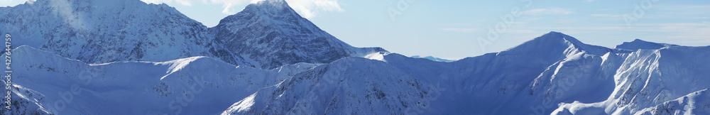 Magnificent panoramic shot of mountain peaks covered in snow during the winter season. A blue sky with few white clouds can be seen in the background. Zakopane - Kasprowy Wierch 