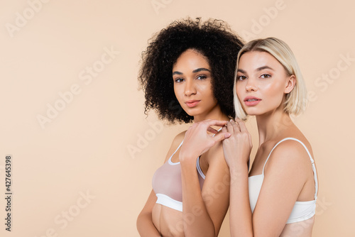 blonde woman touching shoulder of african american friend isolated on beige