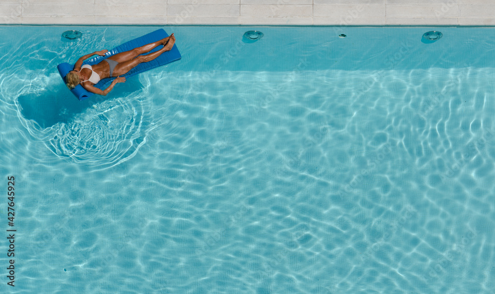 woman sunbathing in bikini in pool on mat