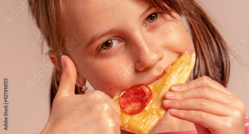It s really delicious  Portrait of cute young girl is eating a piece of pizza. Horizontal image.