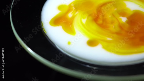 Adding Carotene drops into Cosmetic milk. Mixing white milky liquid and orange beta carotene solution with the wooden spatula. Close up. Rotation. Skincare product for face and body. Beauty concept.