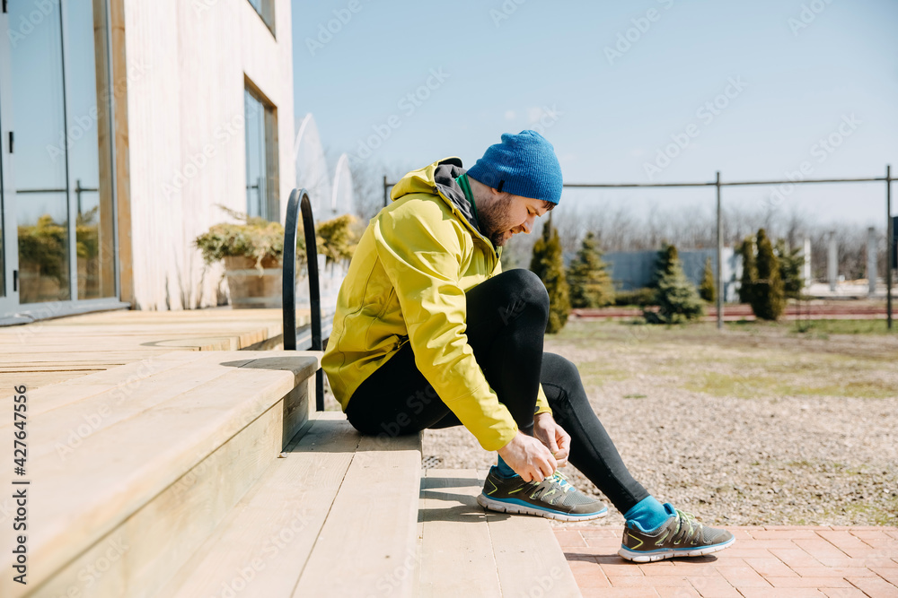 Runner man tying shoelaces on sneakers sitting on wooden stairs, getting ready to run in the morning. Runner man tying shoelaces on sneakers sitting on wooden stairs, getting ready to run in the morning.