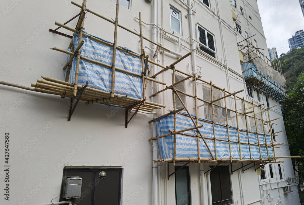 Building wrapped in traditional Chinese scaffolding made of bamboo for worker to repair or replace air conditioner above window outside high rise or the entire building in Hong Kong