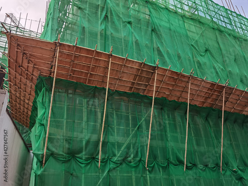 Building wrapped in traditional Chinese scaffolding made of bamboo for worker to repair or replace air conditioner above window outside high rise or the entire building in Hong Kong