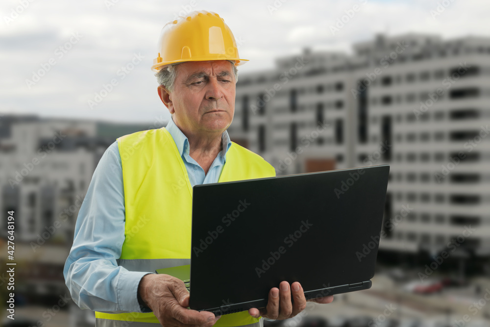 Elderly builder man with focused expression looking at laptop Elderly builder man with focused expression looking at laptop