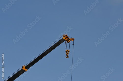Hooks with steel crane slings and arms painted in yellow and black on a blue sky background. Used for lifting large objects or items weighing up to 25 tons. 