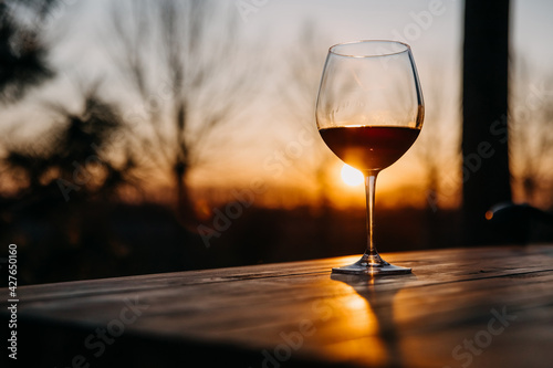 Glass of red wine on a wooden table at a terrace at sunset.