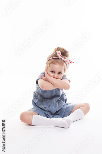 Childhood, emotions concept, little cute girl in a blue dress posing in the studio on a white