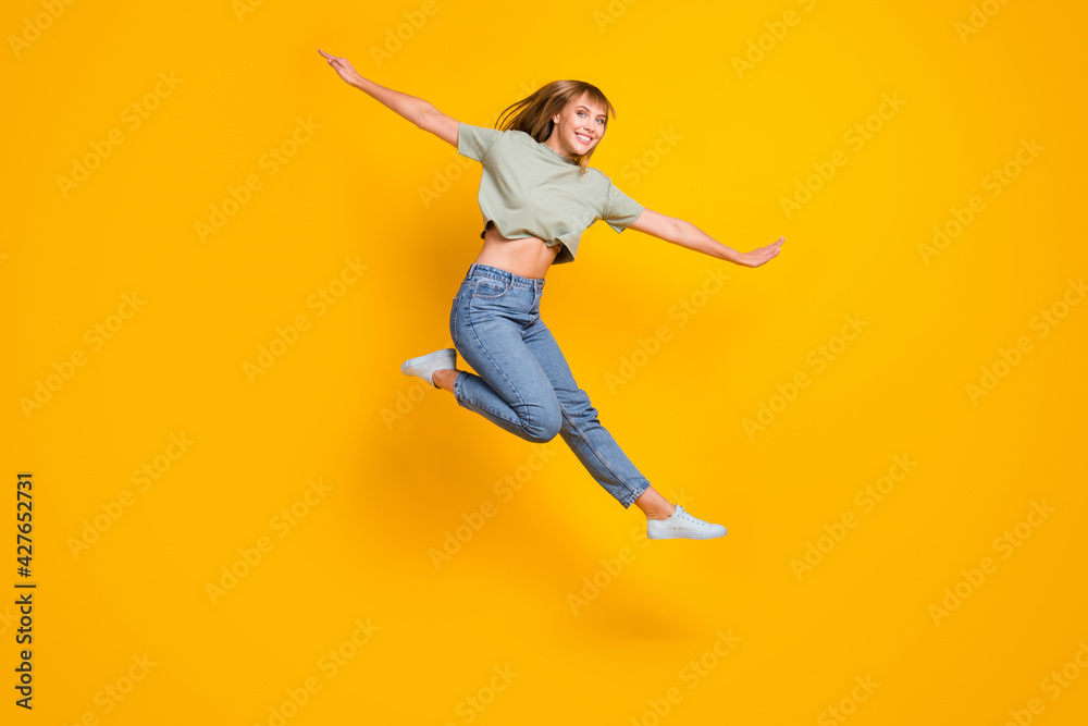 Full length body size view of lovely cheerful girl jumping having fun flying like aircraft isolated over bright yellow color background