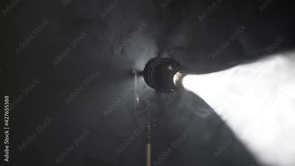 Floodlight beam turns slowly and flares the screen. Stage spotlights and ligth equipment. Spotlight on black background, UHD