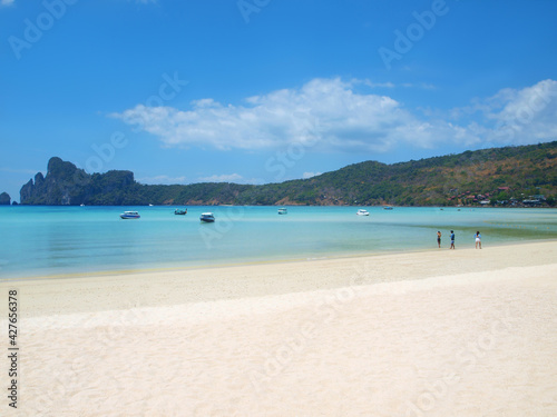 Tropical beach and few people. Boats on the bay. Turquoise sea water. Green hill on the horizon. White sand, blue sky, clouds. Vacation on a resort, rest in paradise. Thailand, Phuket island, Phi-Phi.