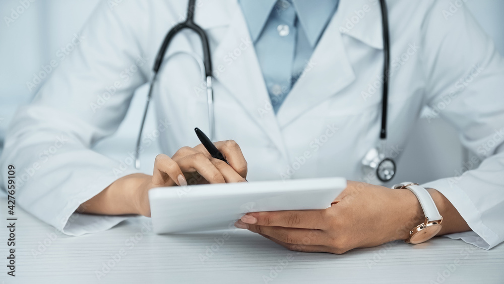 partial view of african american doctor in white coat holding digital tablet partial view of african american doctor in white coat holding digital tablet