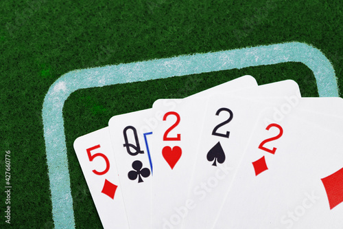 Five playing cards on green textile background top view