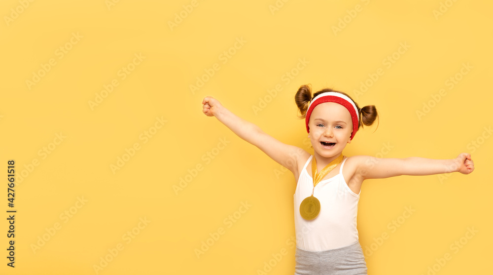 Sport success and win concept - smiling and happy athlete champion child girl celebrates first place victory gold medal award. Sport kid posing over yellow studio background. Banner, mockup,copy space Sport success and win concept - smiling and happy athlete champion child girl celebrates first place victory gold medal award. Sport kid posing over yellow studio background. Banner, mockup,copy space