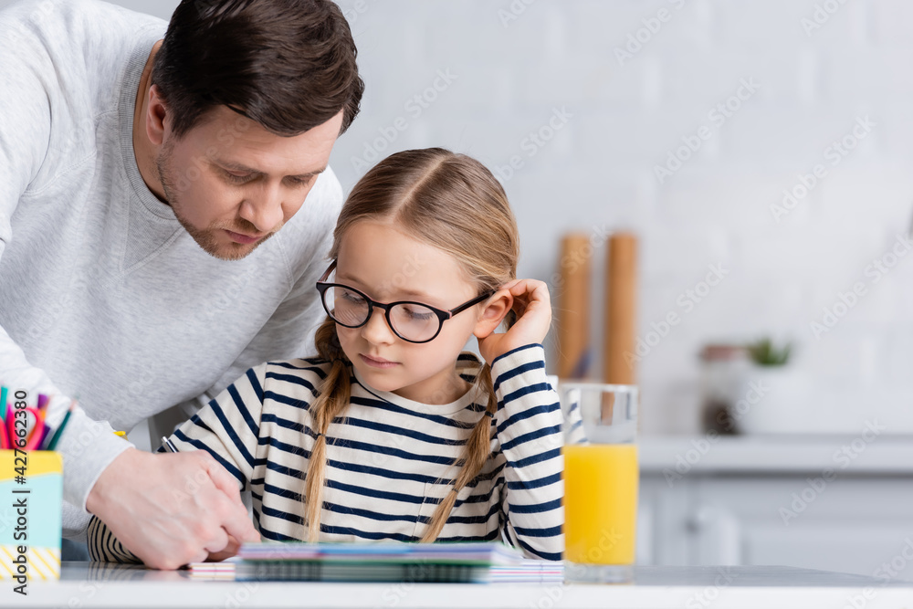 father helping daughter doing homework in kitchen, blurred foreground father helping daughter doing homework in kitchen, blurred foreground